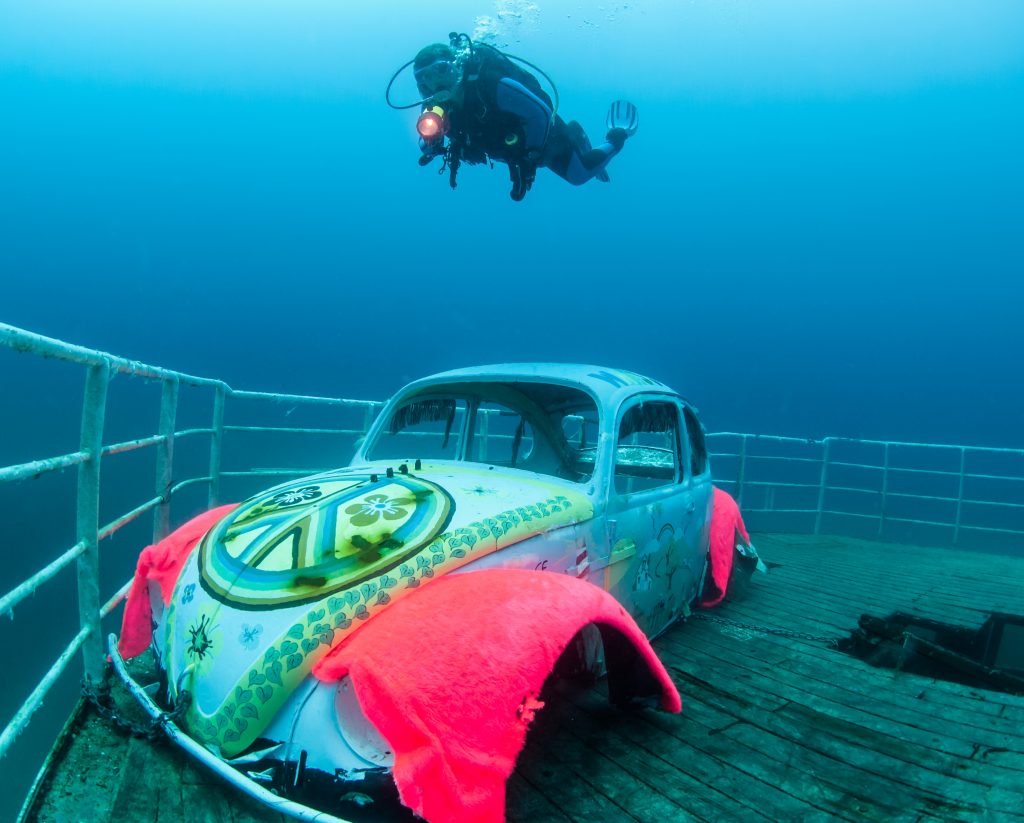 Diver swimming over VW Beetle on submerged wreck